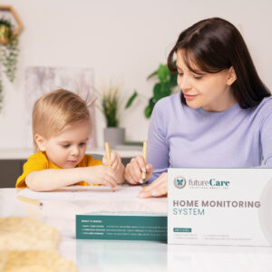 Mother and young child sit at a white table drawing together, with a FutureCare Home Monitoring System box in the foreground.